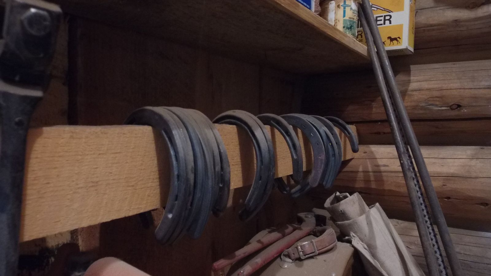 A row of used horseshoes hung along a wooden rail beside farrier tools